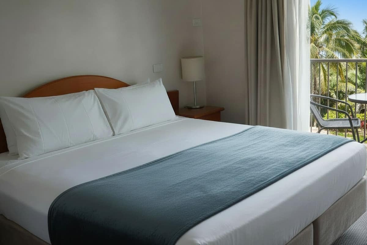 A hotel room with a large bed, a nightstand, a lamp, and a balcony with a table and chairs.