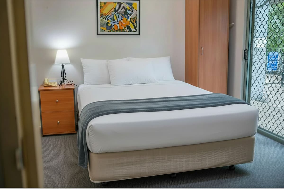 A hotel room with a bed, a nightstand, a lamp, a painting on the wall, and a view through a glass door.