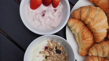 A table with two bowls of food, one with yogurt and strawberries, and the other with yogurt and granola. There are also several croissants on a plate.