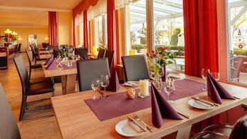 Un restaurante con mesas de madera dispuestas para comer, cortinas rojas y ventanas amplias.