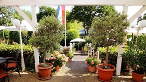 An outdoor patio area with potted plants, a white pergola, and a white fence in the background. - Park Hotel (Traben-Trarbach)