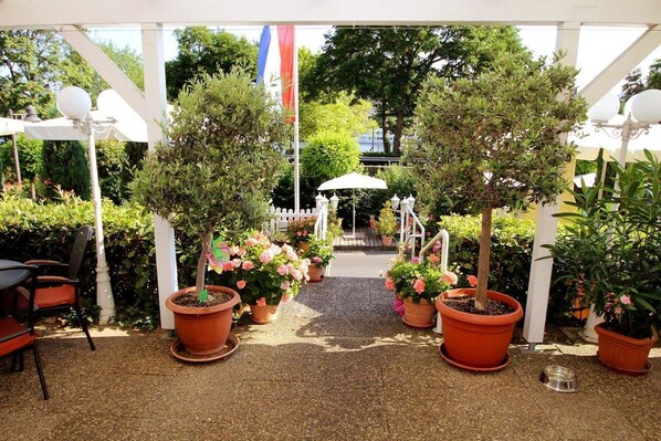 Un patio al aire libre con plantas en macetas, una pérgola blanca y una valla blanca al fondo.