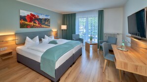 A hotel room with a bed, a desk, a chair, a TV, and a painting on the wall. - Park Hotel (Traben-Trarbach)
