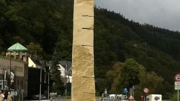 Ein hohes Steins Denkmal mit einem geschnitzten Kopf an der Spitze, gelegen in einer grünen Anlage mit einer Straße und Fahrzeugen im Hintergrund.