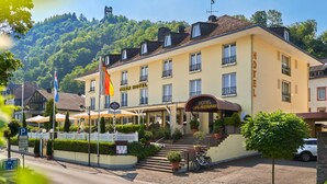 A hotel with a cafe and restaurant, surrounded by greenery and a hill in the background. - Park Hotel (Traben-Trarbach)