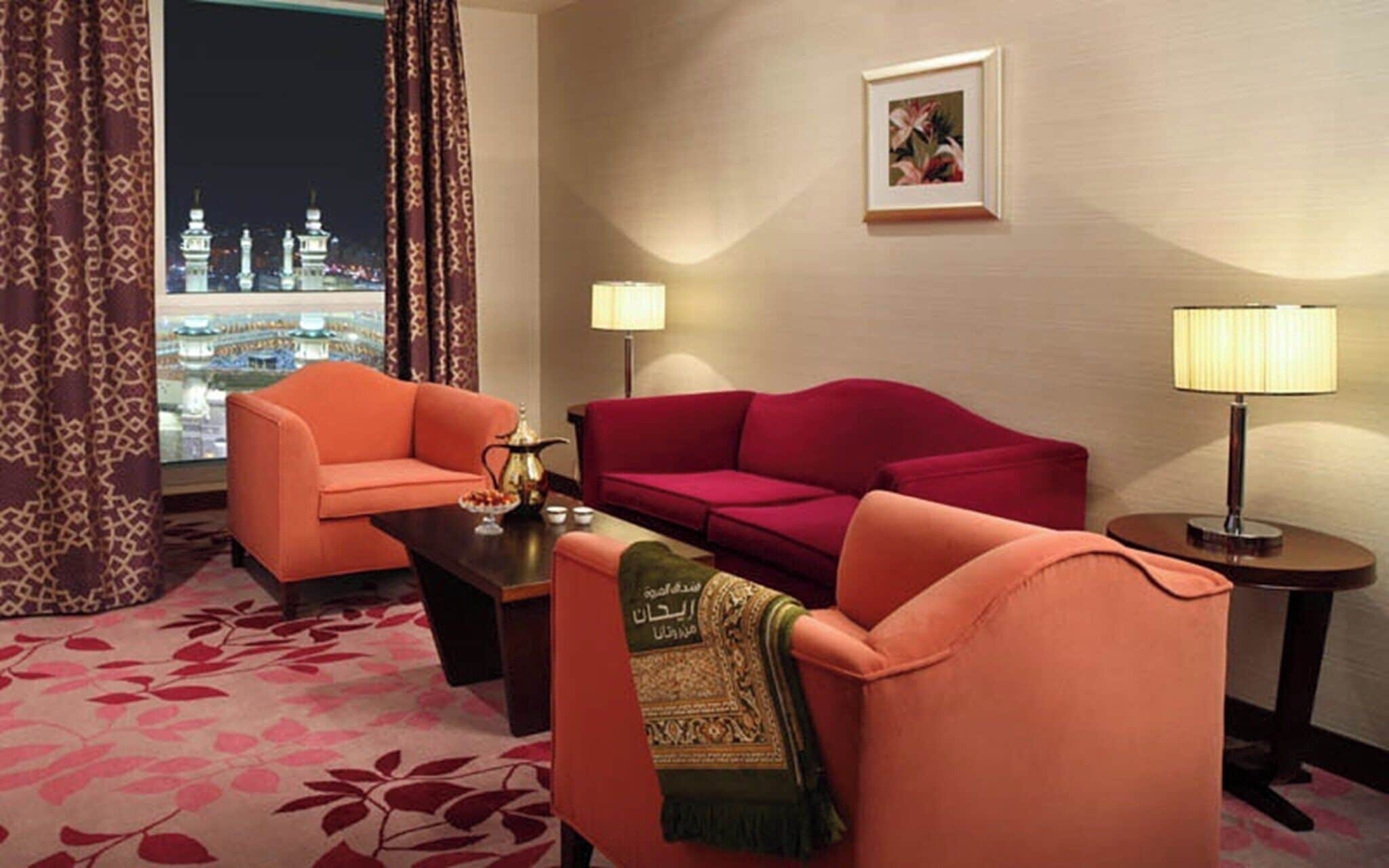 A hotel room with a view of a cityscape at night, featuring two sofas and two lamps.