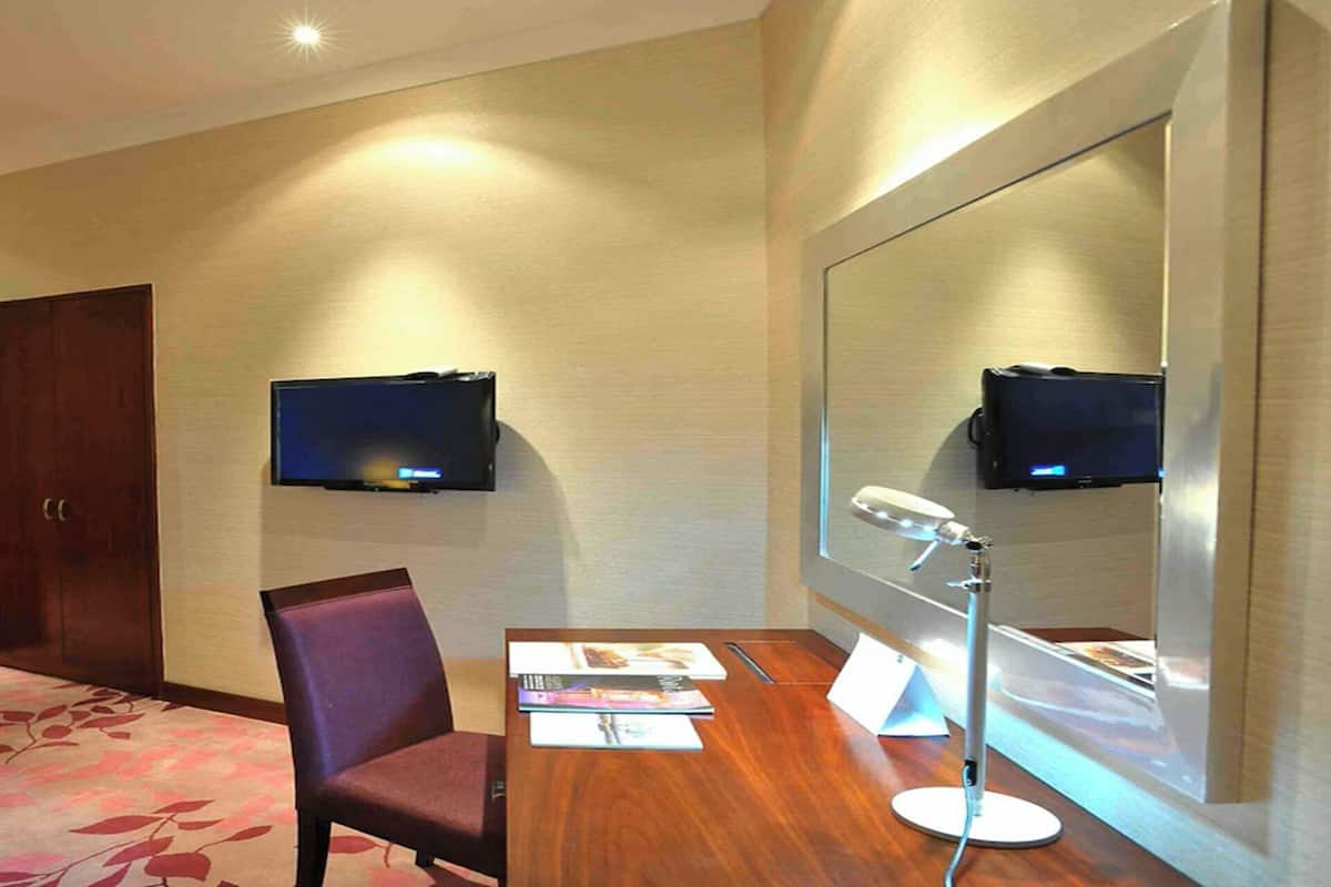 Habitación de hotel con cama, escritorio y silla, televisor de pantalla plana montado en la pared, espejo grande y lámpara de escritorio.