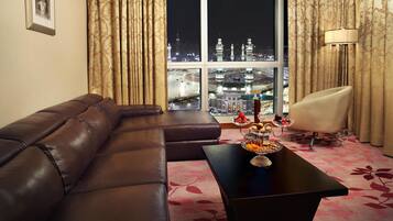 A modern living room with a leather sofa, a dining table with fruit, and a view of a cityscape at night.