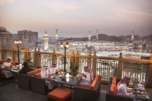 A rooftop dining area with a view of a large mosque and surrounding buildings. - Al Marwa Rayhaan by Rotana (Makkah)