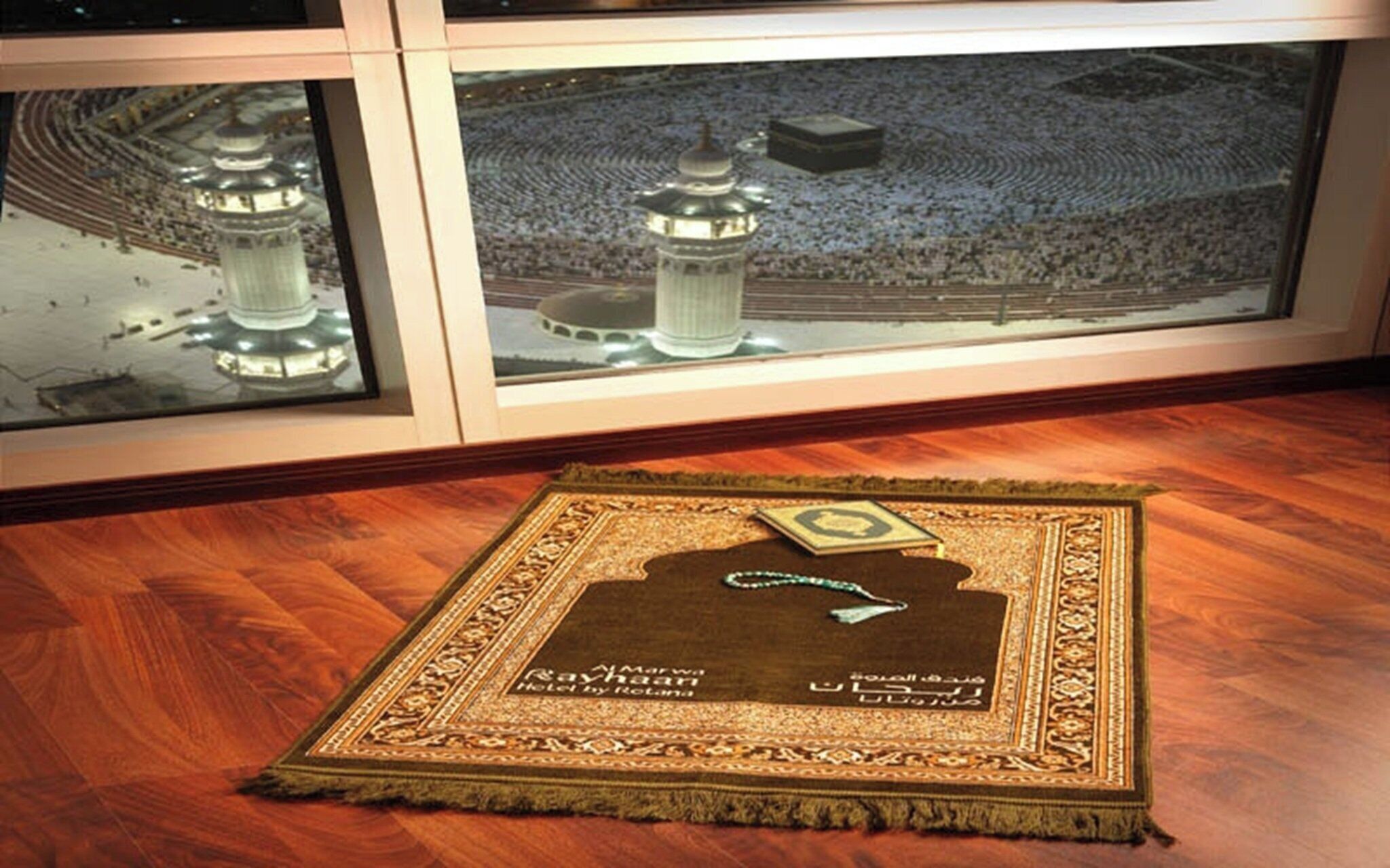 A room with a wooden floor, a framed photograph of a mosque, and a decorative rug with Arabic script.