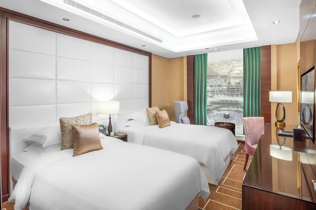 Habitación de hotel con dos camas, un ventanal con vistas, un escritorio con lámpara y un televisor.