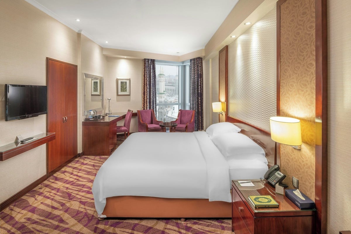 Una habitación de hotel con una cama grande, un escritorio con teléfono, una silla, un televisor y una ventana con vista a la ciudad.