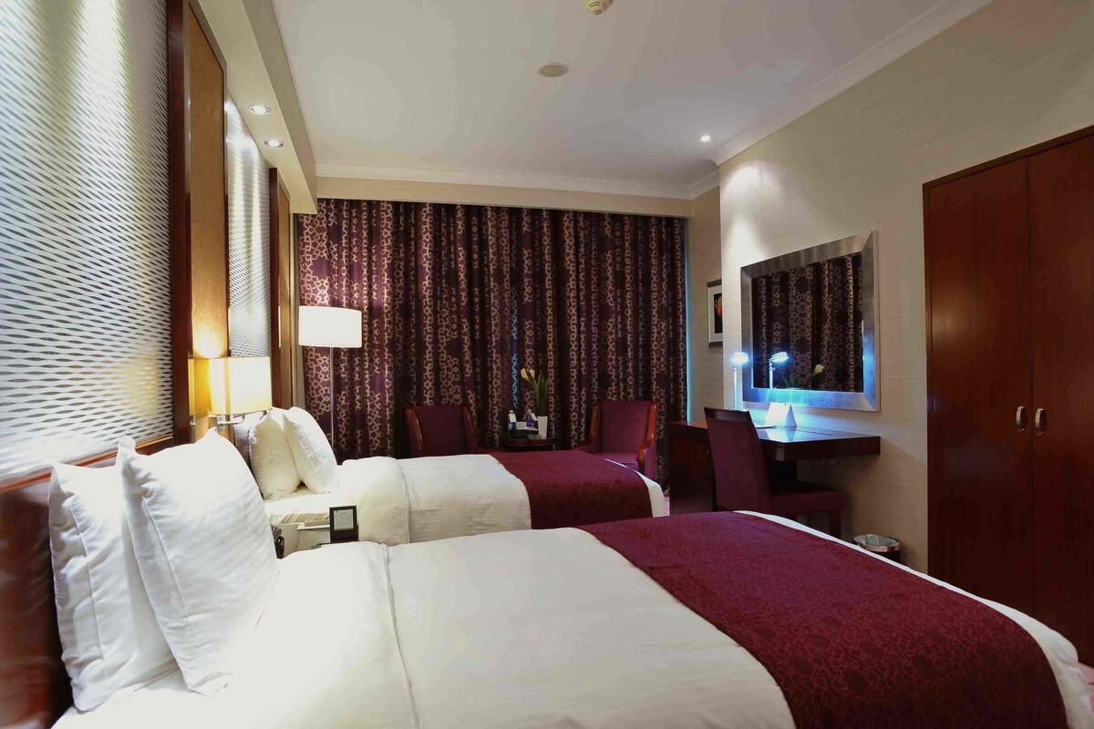 A hotel room with two beds, a desk, a TV, and a wardrobe.