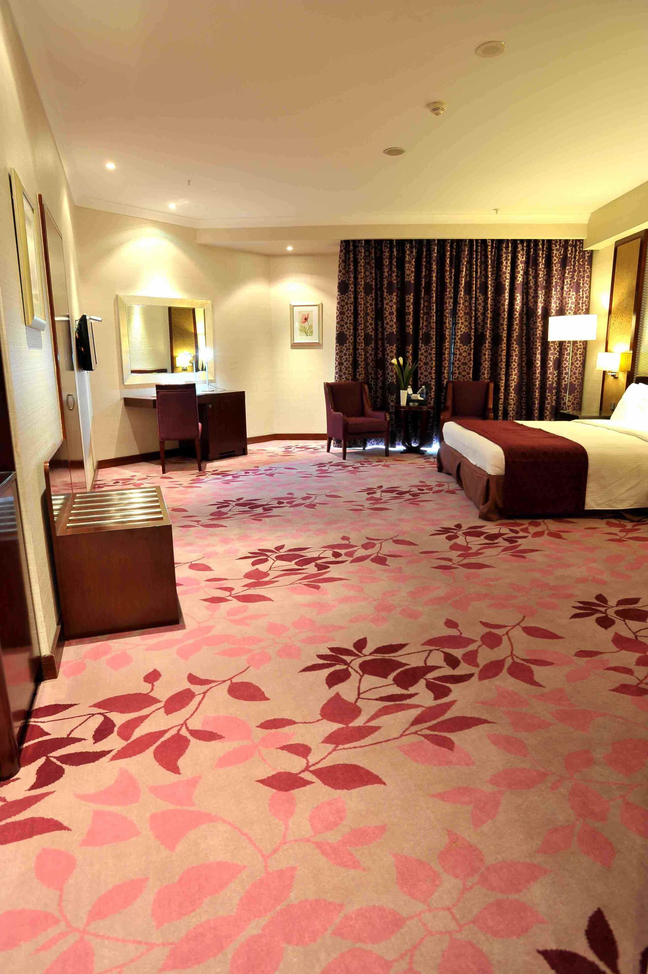 Quarto de hotel com cama, escrivaninha, cadeira e um espelho grande.