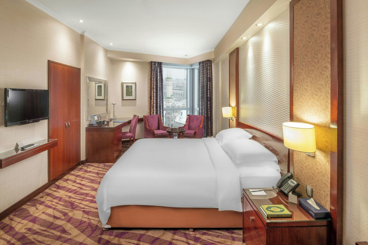 Une chambre d’hôtel avec un grand lit, un bureau avec un téléphone, une télévision et une vue sur le paysage urbain par la fenêtre.