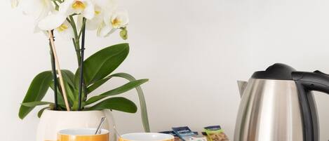 Een keukentafel met een koffiezetapparaat, twee gele mokken, een kamerplant en een televisie erboven.