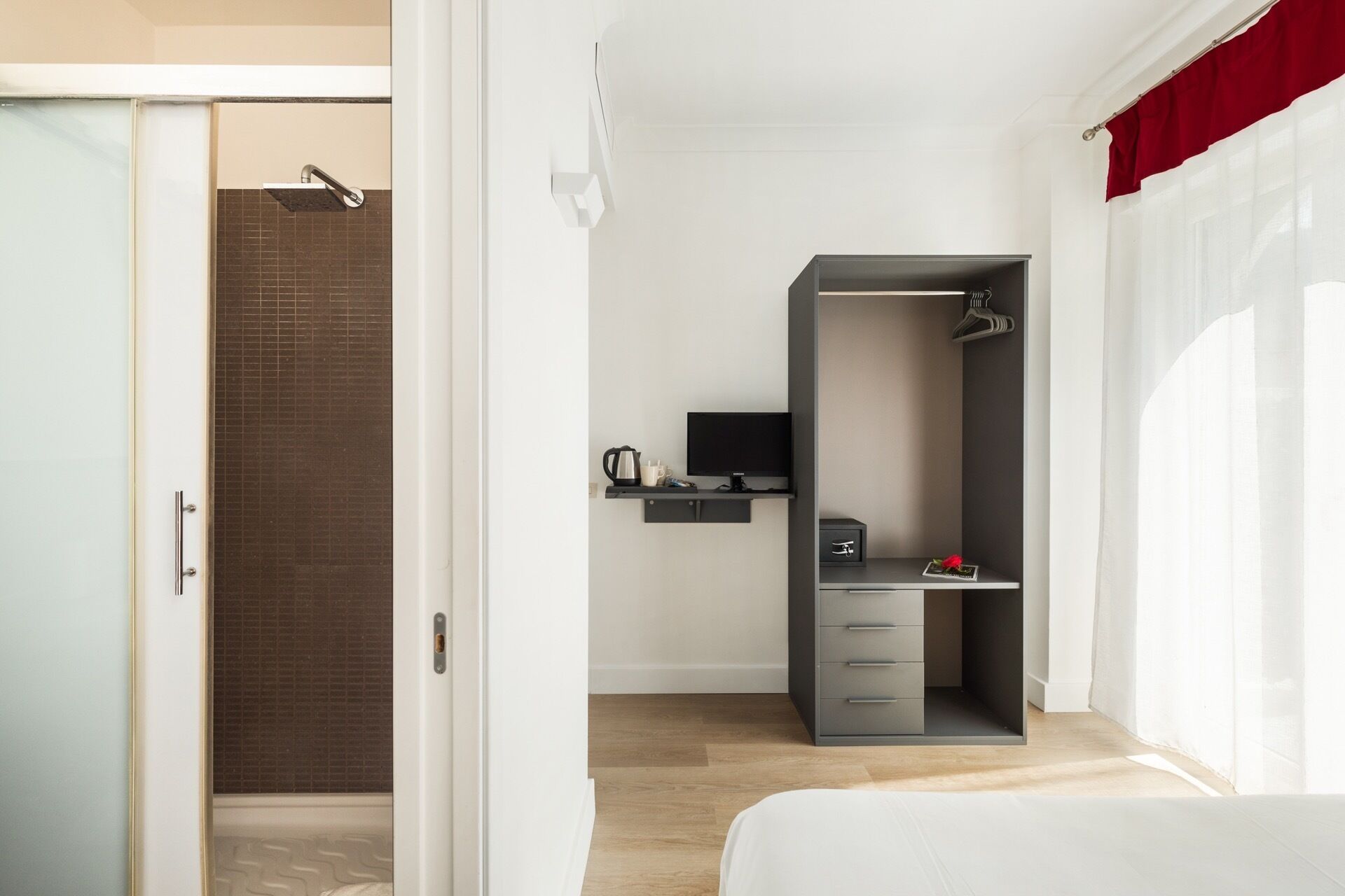 A modern hotel room with a shower, a desk with a computer, and a bed.