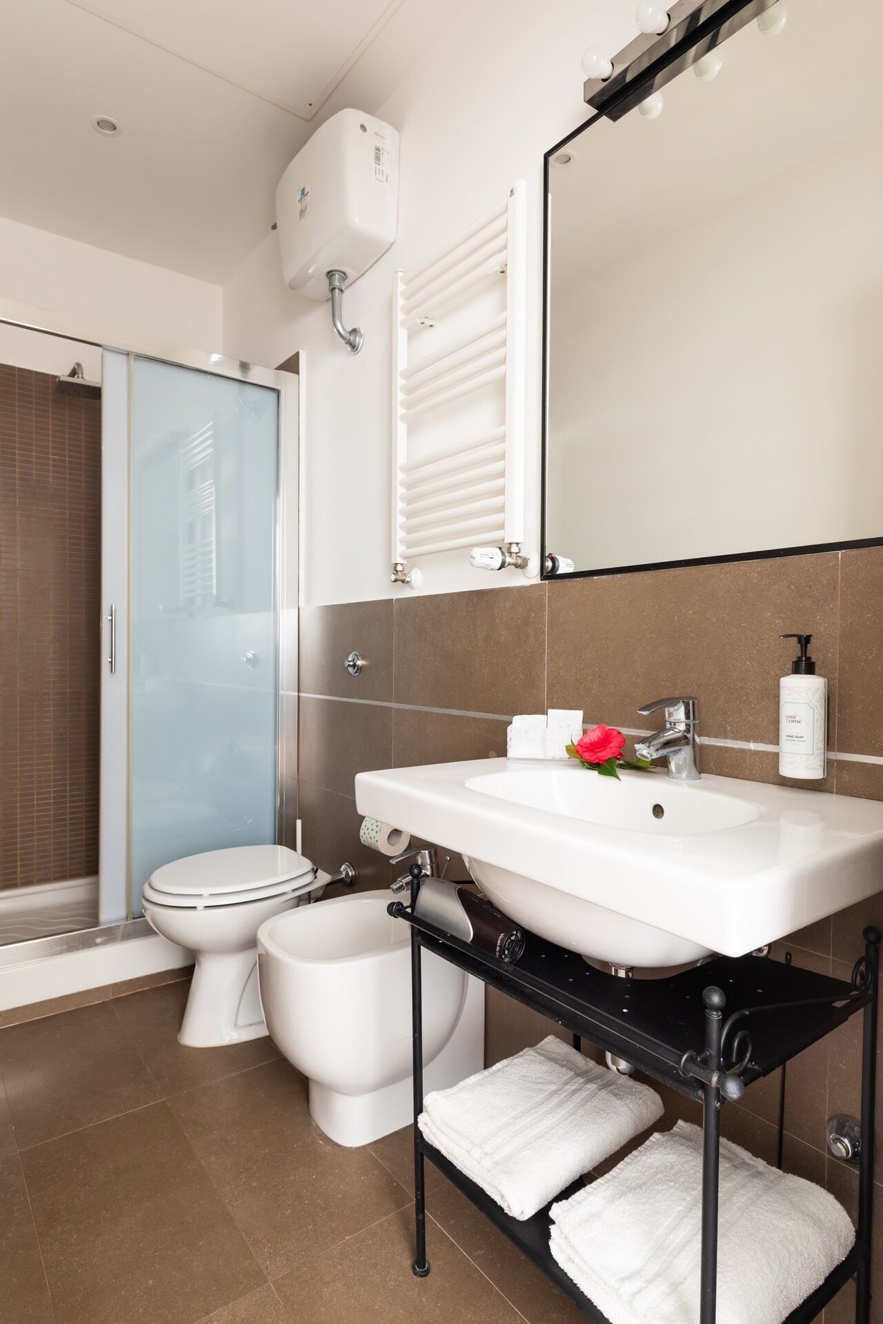 A modern bathroom with a glass shower enclosure, a white sink with a black shelf, and a large mirror.