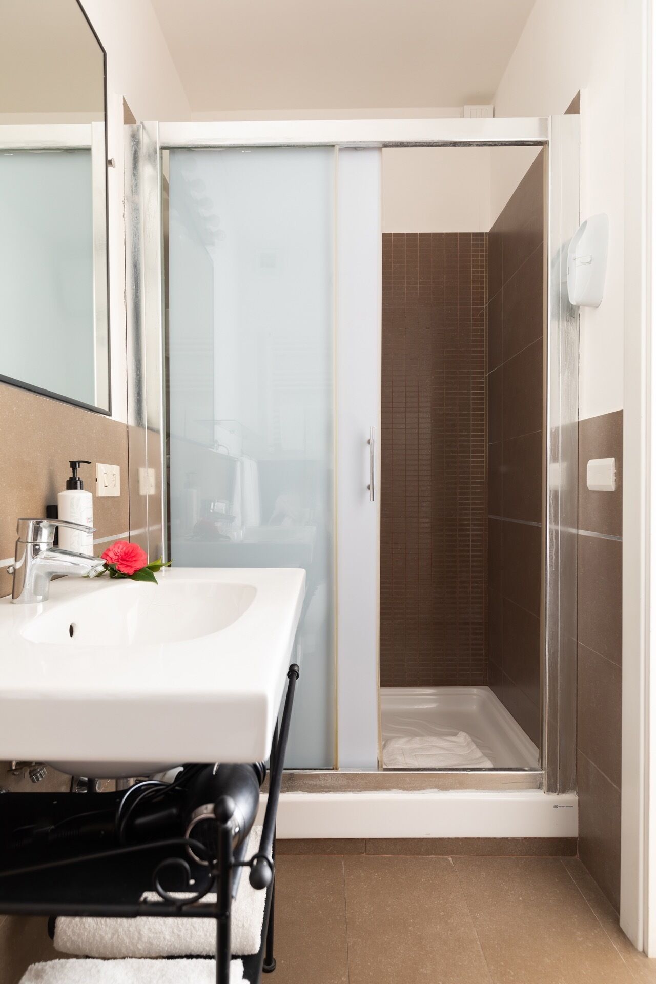 Een badkamer met een witte wastafel, een douchecabine van glas en een spiegel.