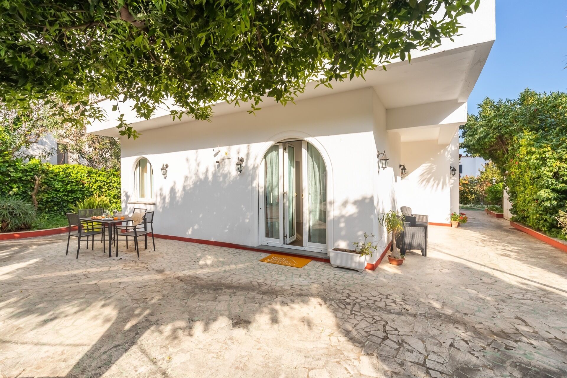 Un edificio moderno con un patio cubierto, mobiliario exterior y plantas en macetas.