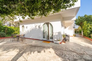 Un edificio moderno con un patio cubierto, mobiliario exterior y plantas en macetas.