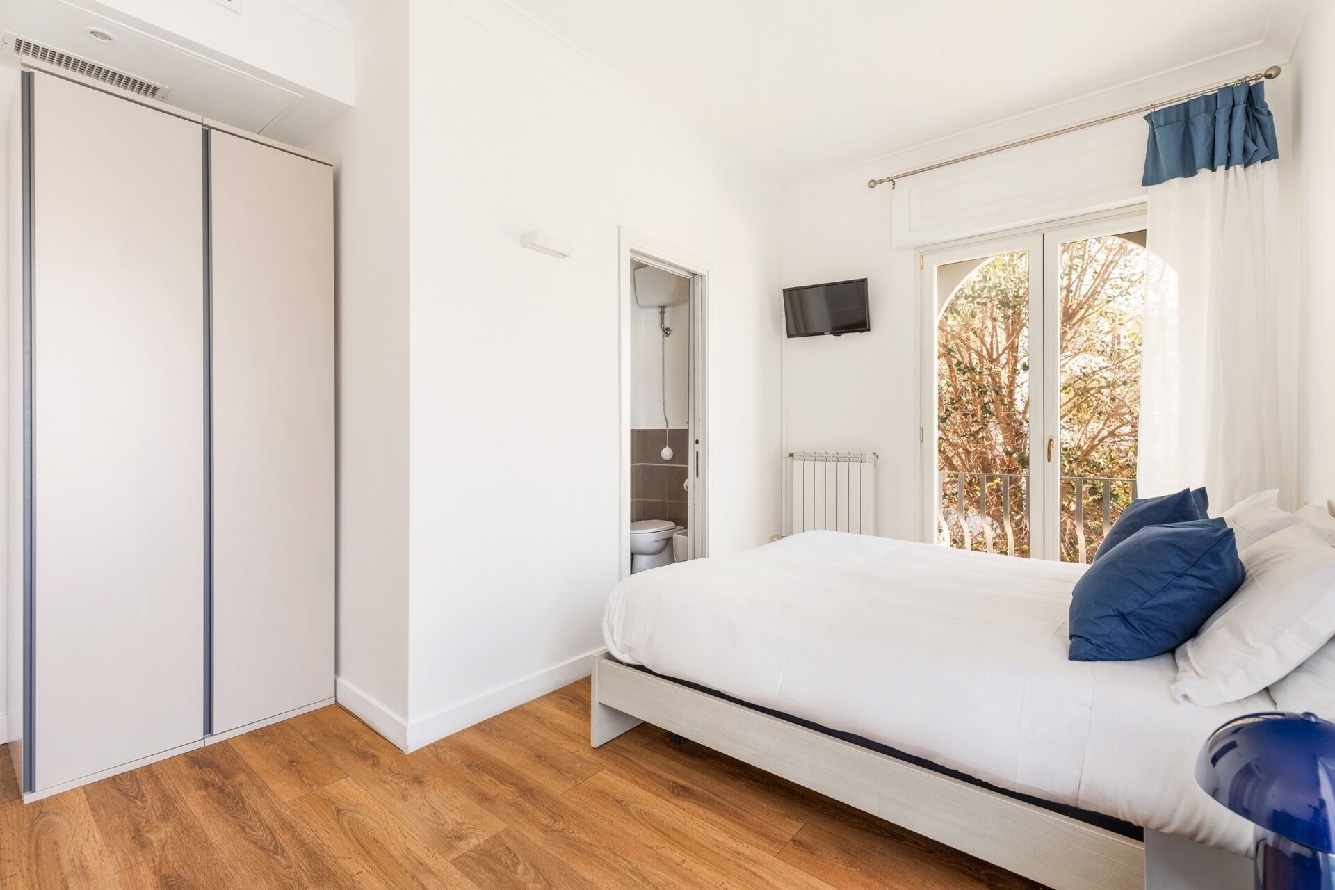 Un dormitorio con cama, armario, televisor y ventana con cortinas.