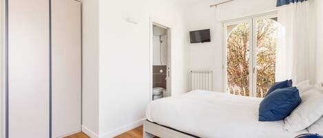 Un dormitorio con cama, armario, televisor y ventana con cortinas.