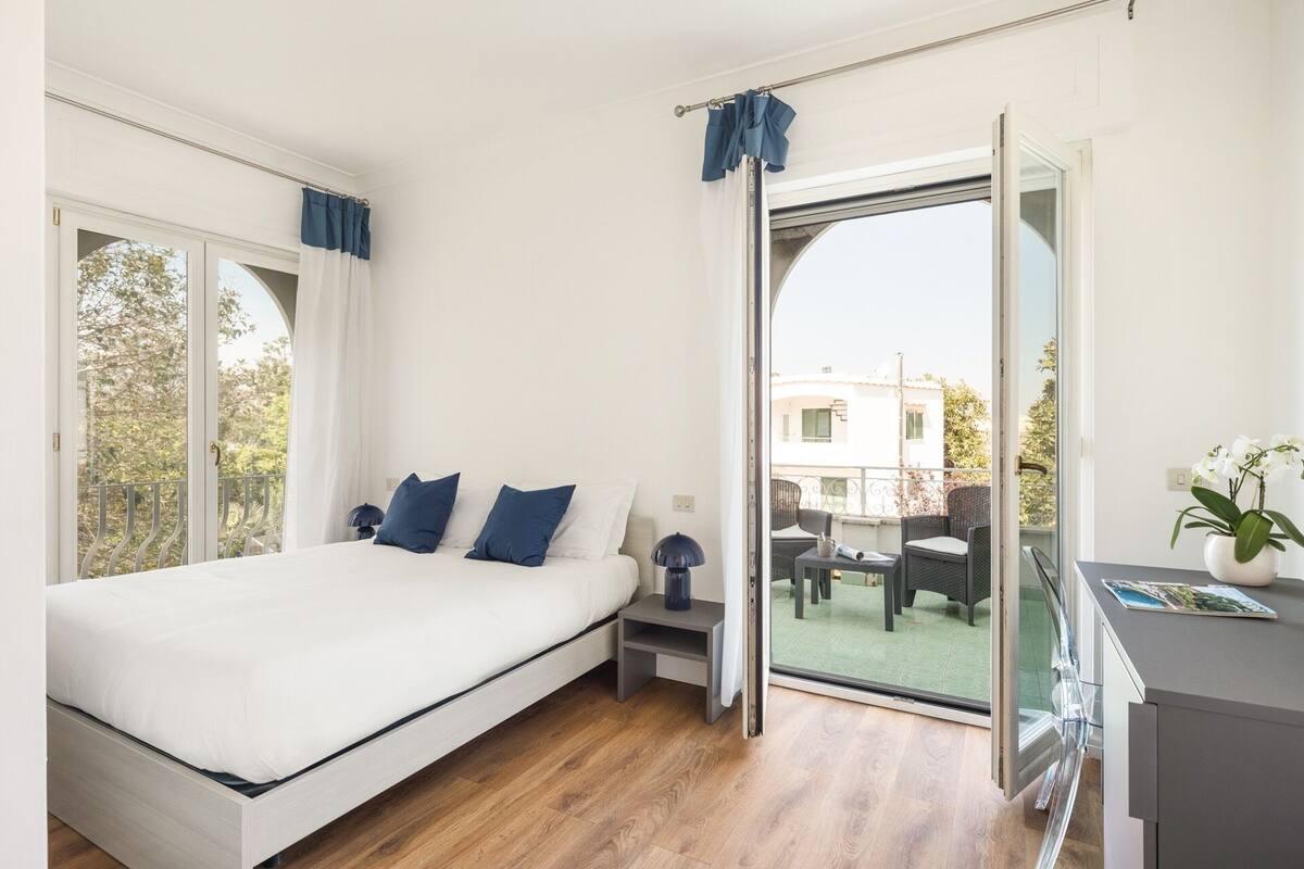 A bedroom with a bed, a nightstand, a lamp, and a view of the outside balcony.