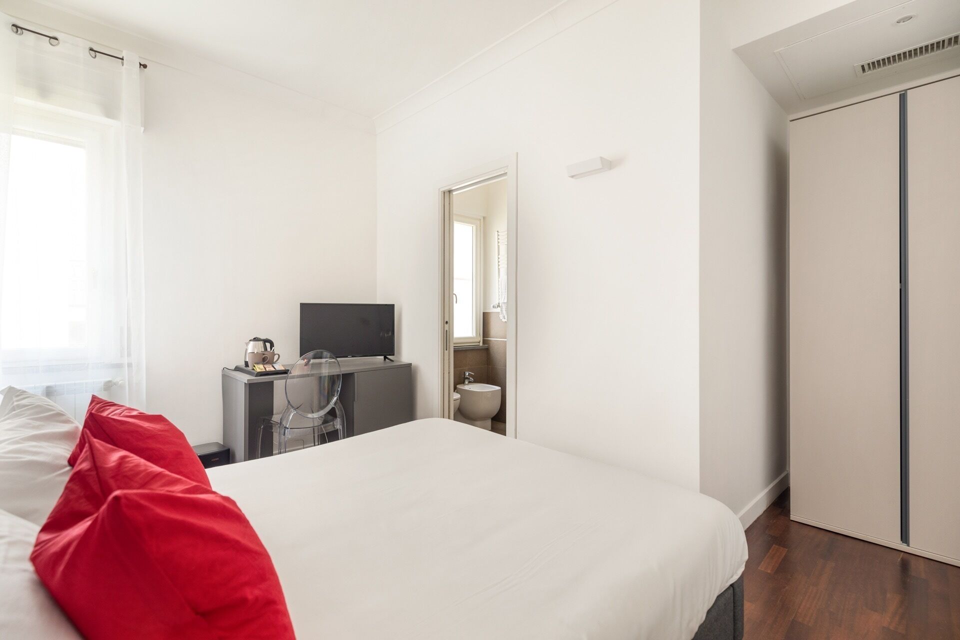 A hotel room with a bed, a desk with a television, a bathroom, and a wardrobe.