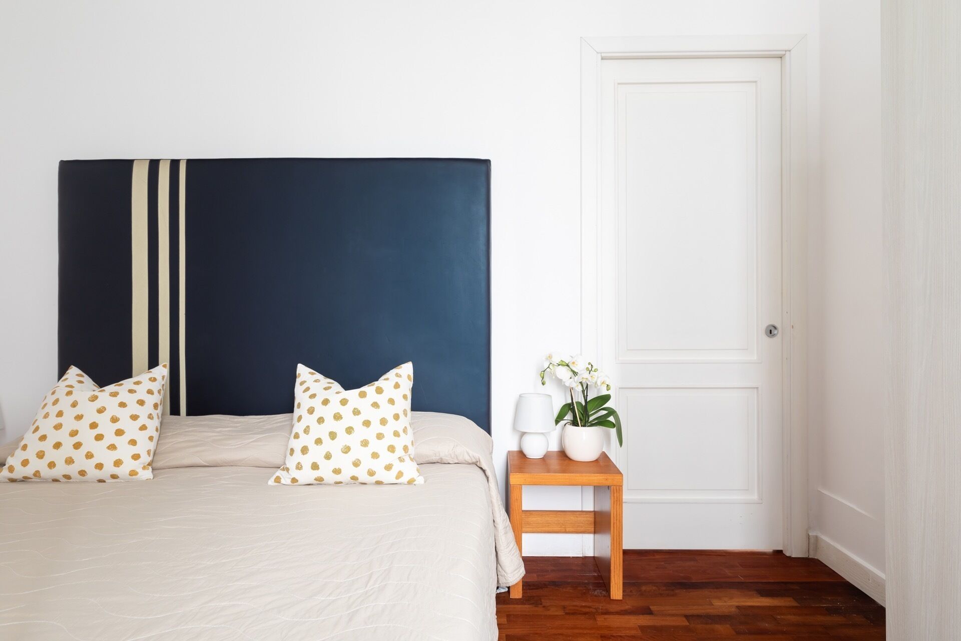 A bedroom with a bed, pillows, a bedside table with a lamp, and a door.