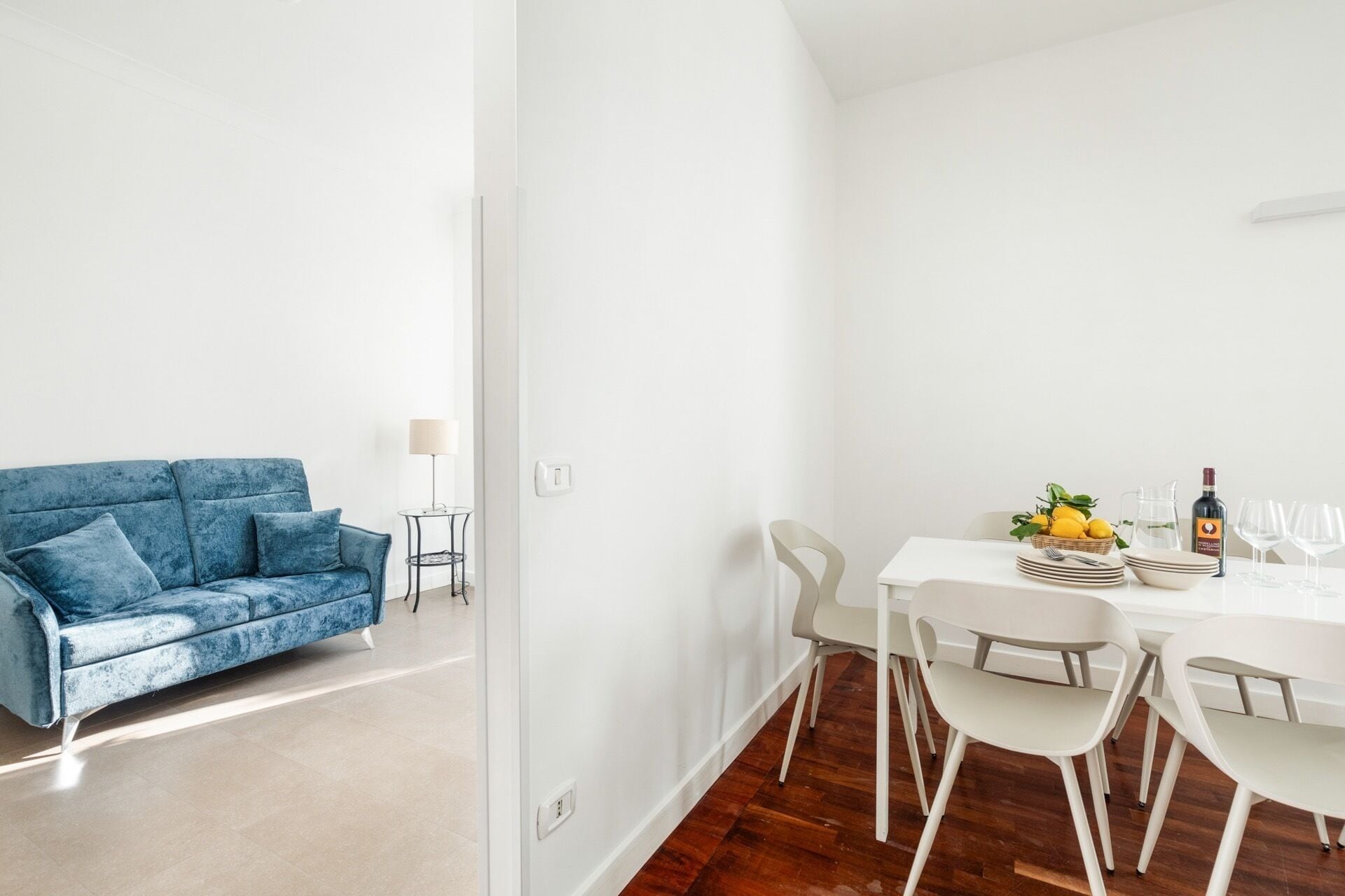 Un salon moderne avec un canapé bleu et un coin repas comprenant une table et des chaises blanches.