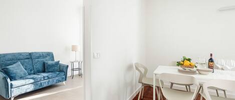 Un salon moderne avec un canapé bleu et un coin repas comprenant une table et des chaises blanches.