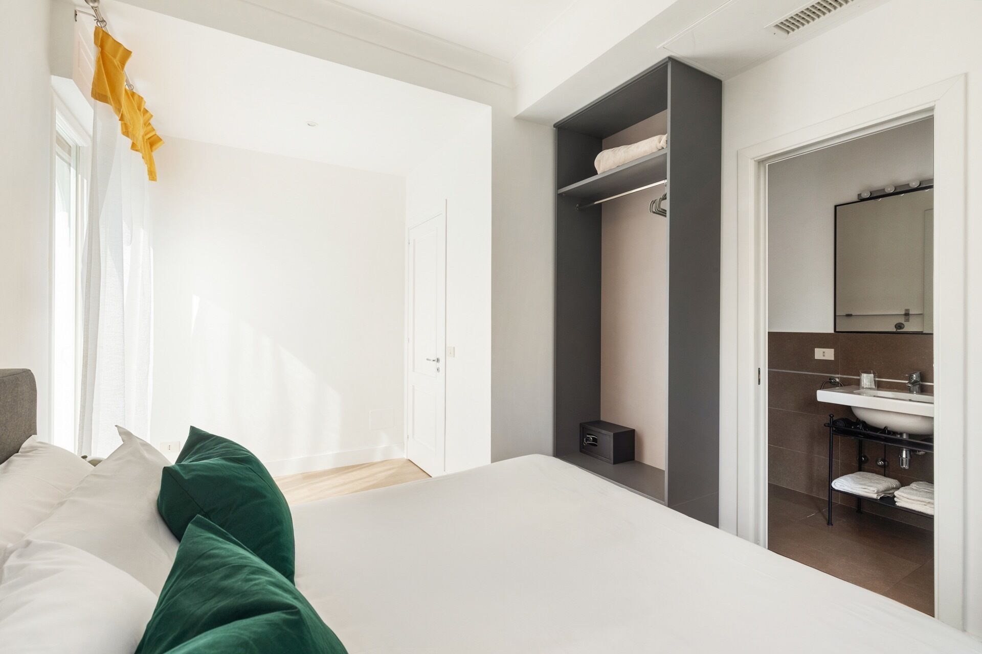 Une chambre moderne avec un grand lit, une armoire et une salle de bain équipée d’un lavabo et d’un miroir.