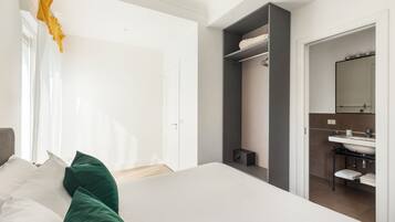 Une chambre moderne avec un grand lit, une armoire et une salle de bain équipée d’un lavabo et d’un miroir.