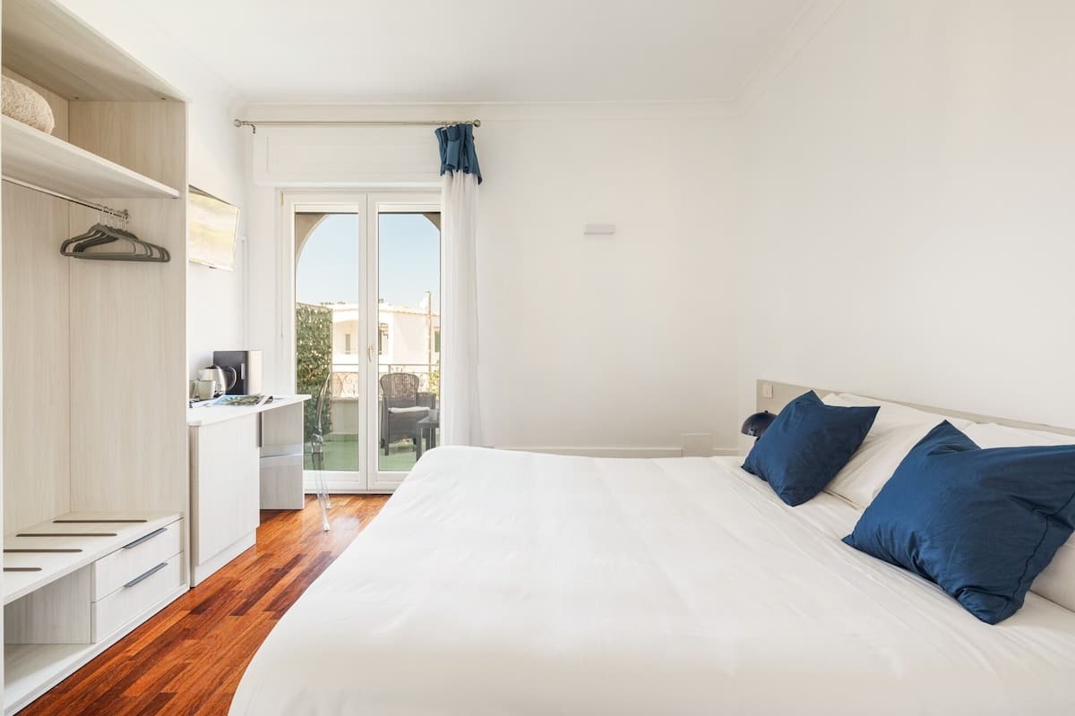 A bedroom with a large bed, a wardrobe, a desk, and a view of the outside.