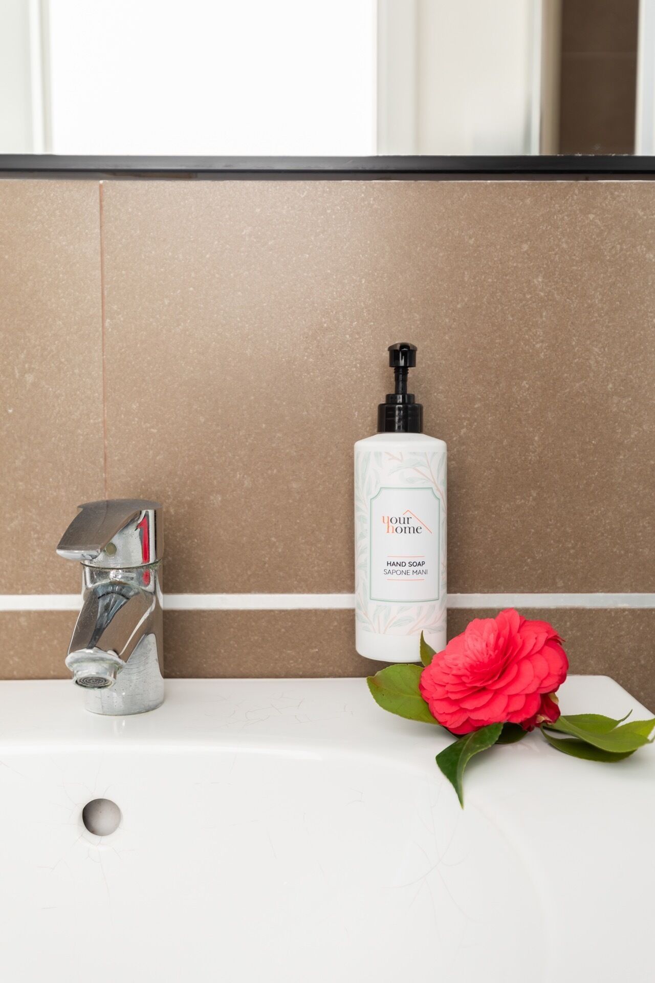 A bathroom sink with a chrome faucet, a bottle of hand soap, and a red flower on the counter.