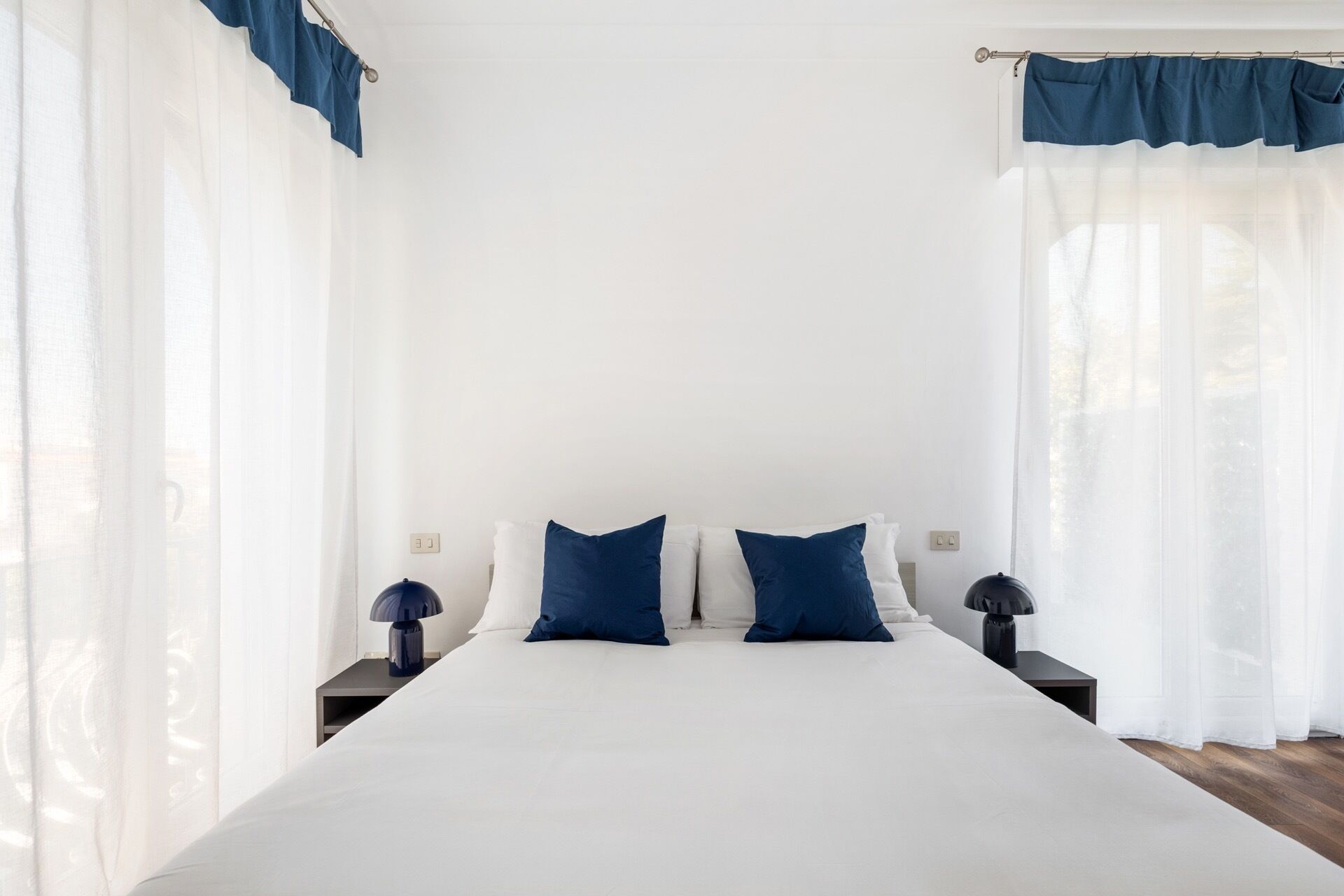 A bedroom with a large bed, two bedside tables, and a window with sheer curtains.