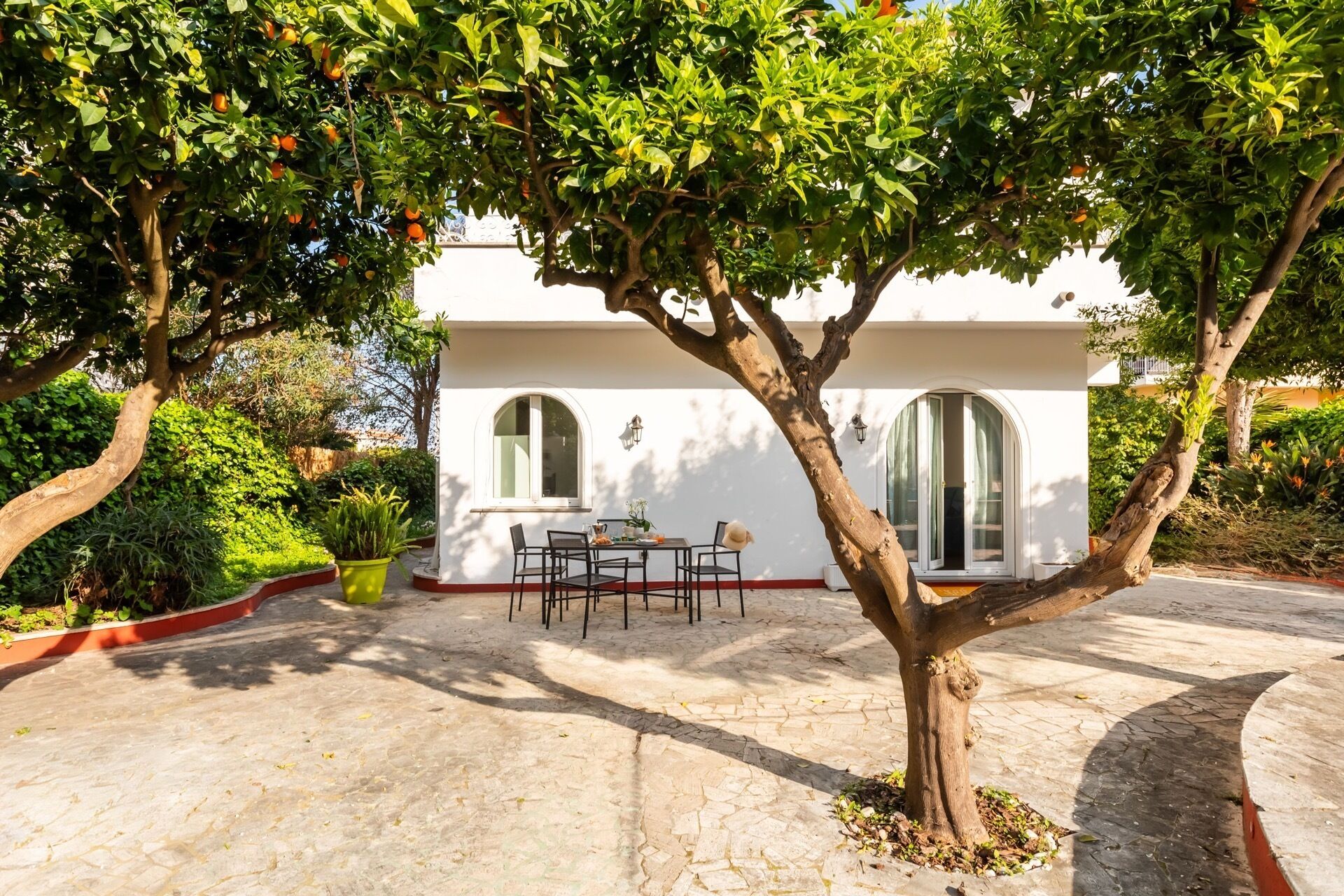 A white building with a patio, a table with chairs, and a tree with fruit.