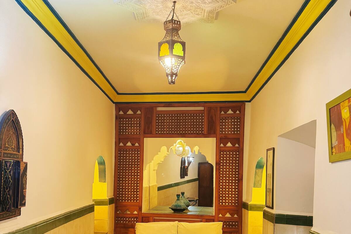 A room with a bed, a small table, a mirror, and a hanging light fixture.