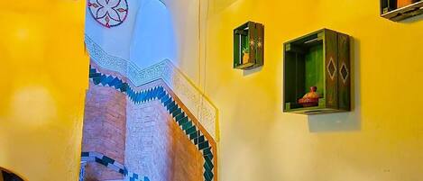 A staircase with patterned tiles, a hanging light fixture, and a small potted plant on the wall.