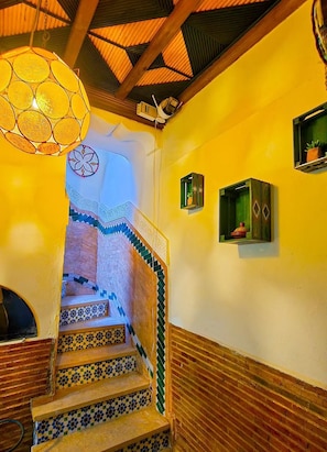 A staircase with patterned tiles, a hanging light fixture, and a small potted plant on the wall.