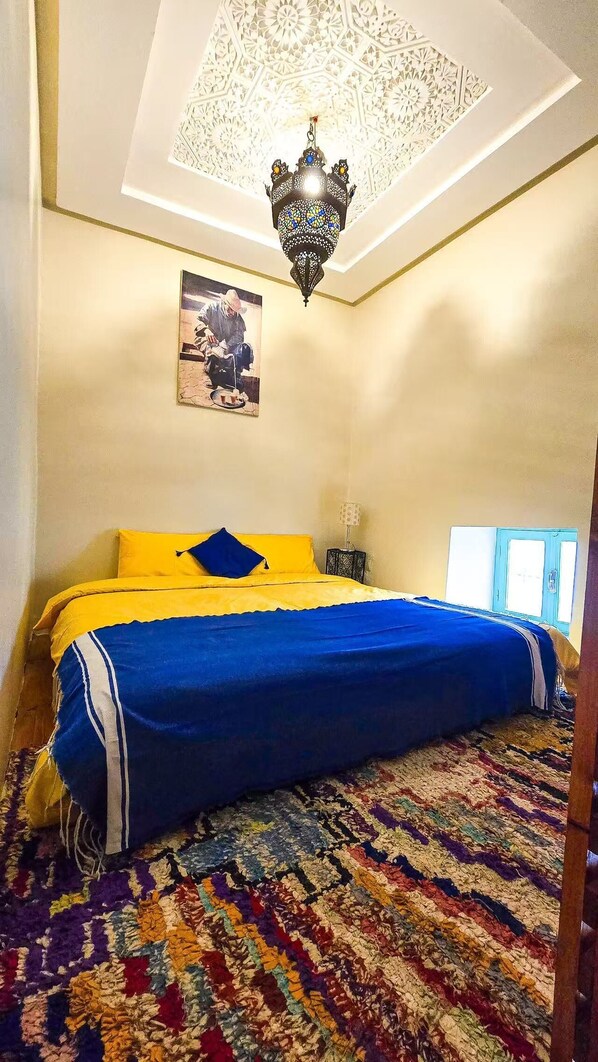 A bedroom with a bed, a patterned rug, a hanging light fixture, and a painting on the wall. - Riad Zara (Marrakech)