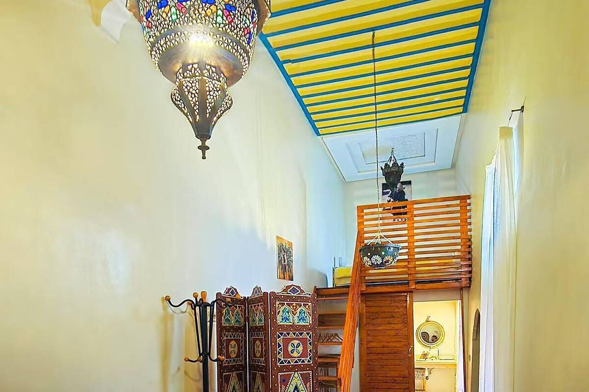 A bedroom with a bed, a hanging light fixture, a wardrobe, and a wooden door.