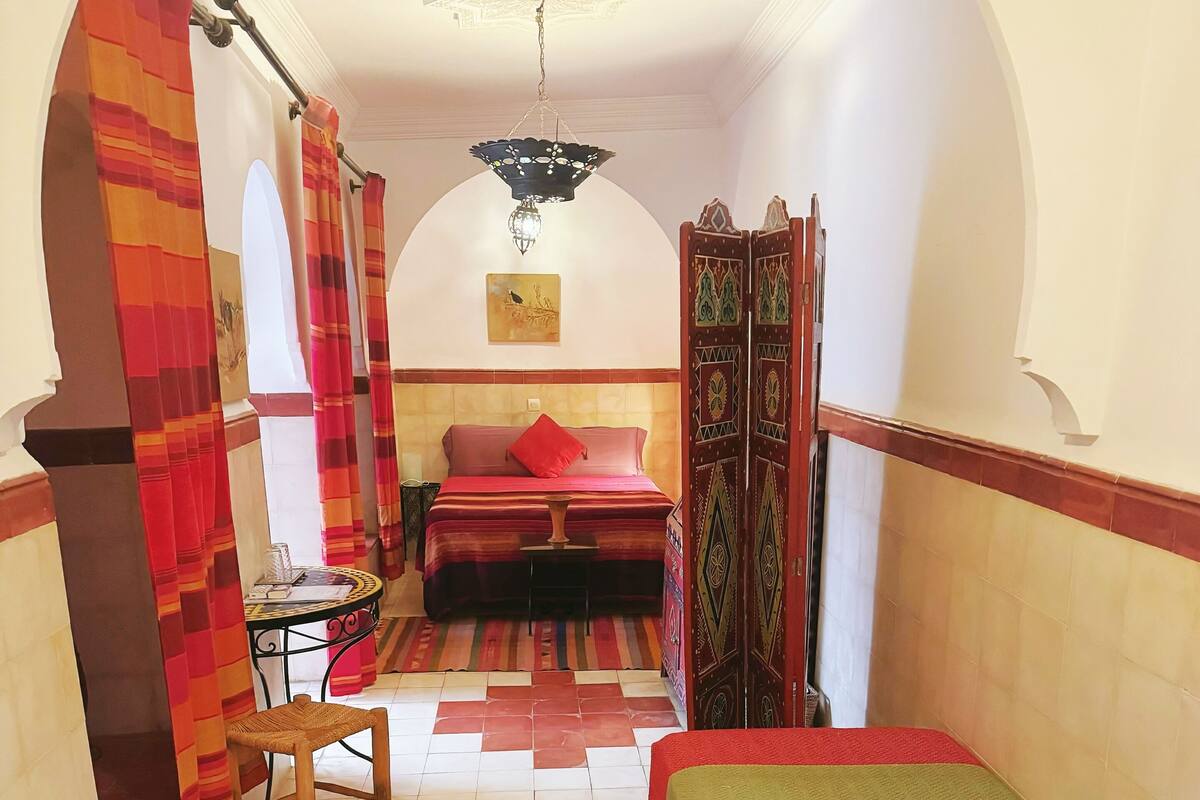 A room with a bed, a small table, a chair, and a decorative door.