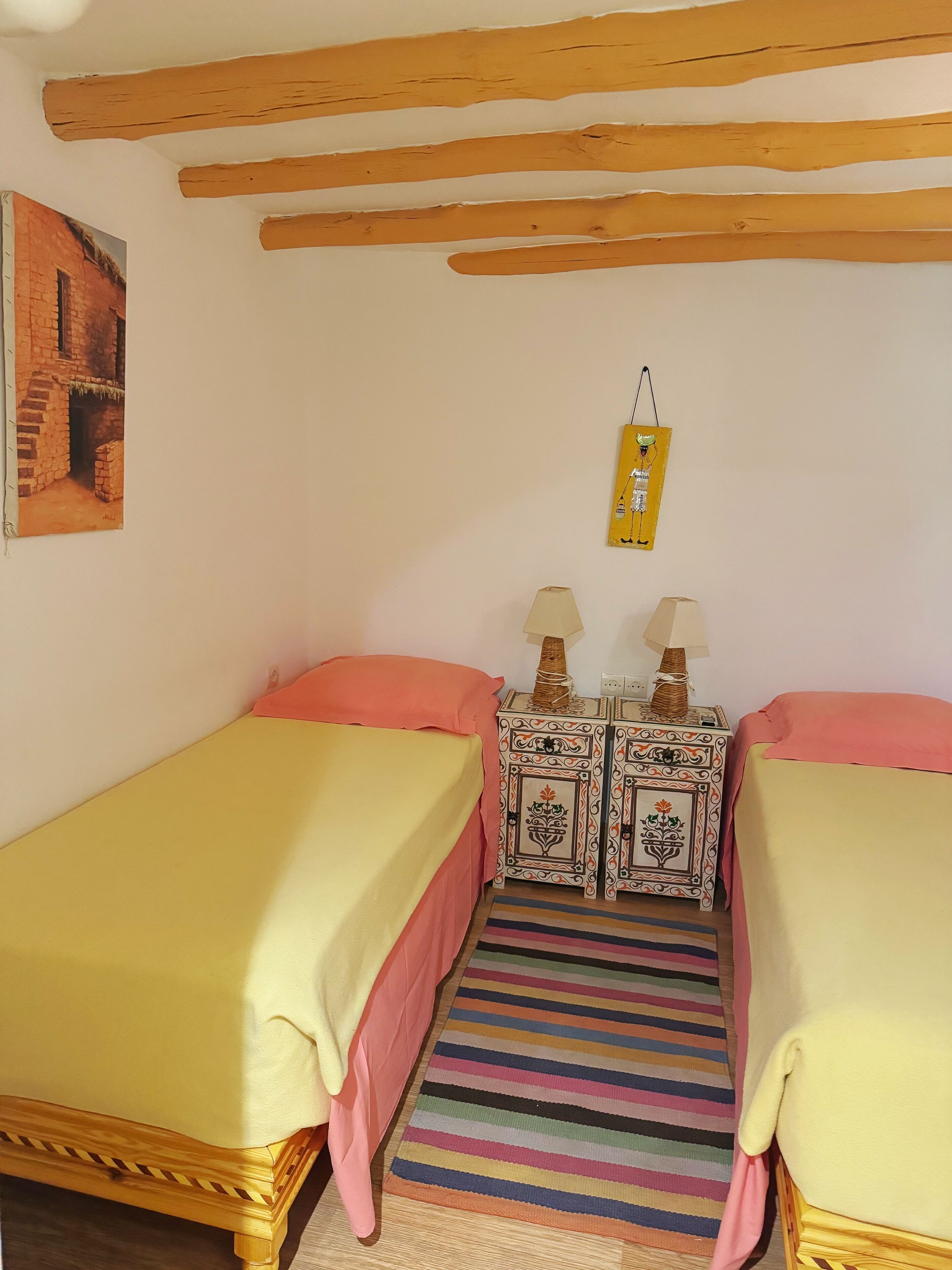 A bedroom with two beds, a striped rug, and a small table with lamps.