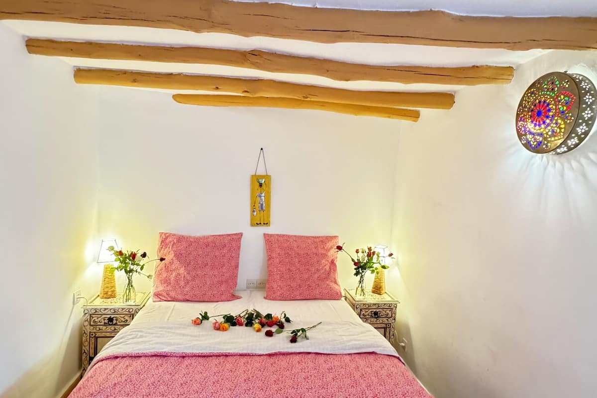 A bedroom with a bed, two bedside tables, a wall decoration, and a ceiling beam.