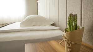 Ein Bett mit weißer Bettwäsche, ein Nachttisch aus Holz und eine Papiertüte mit einer Pflanze darauf.