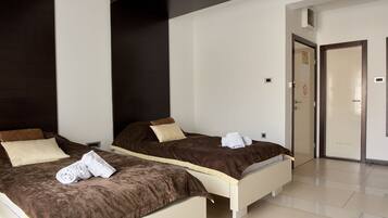 A hotel room with two beds, each with a brown headboard, white bedding, and a rolled towel on the bed.