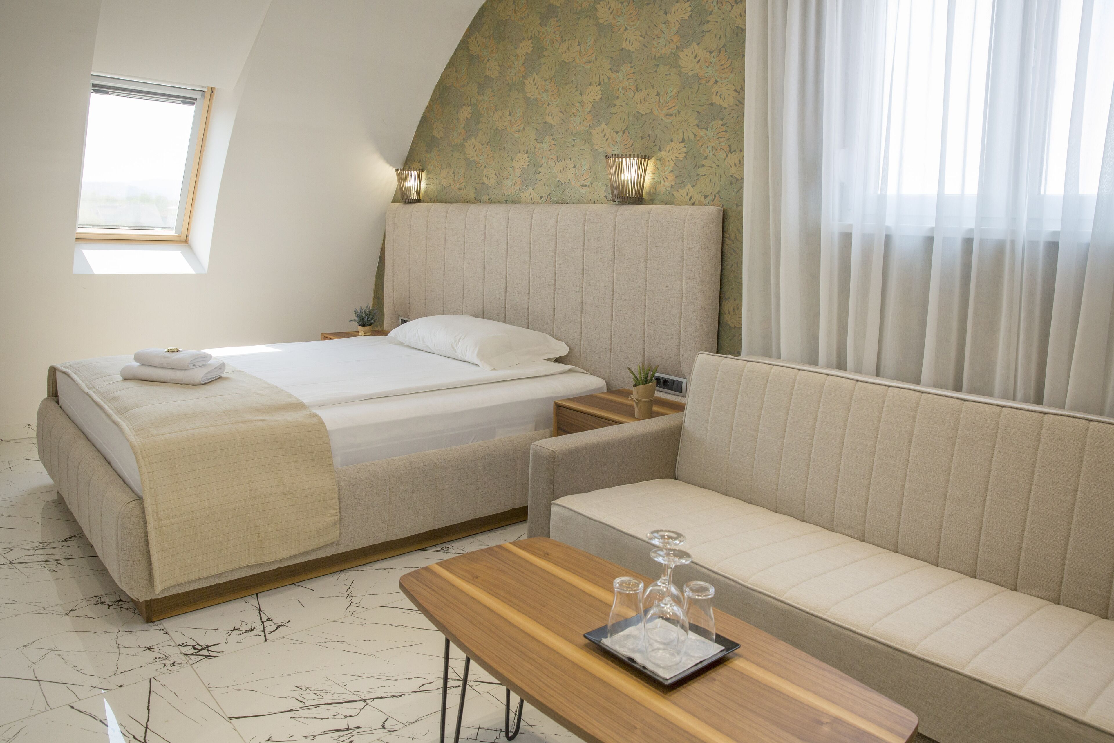 A bedroom with a bed, a sofa, a wooden table, and a window.