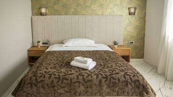 Un lit bien fait, avec une couvre-lit à motifs et une serviette pliée posée sur le côté. Il y a deux tables de chevet avec des lampes et un luminaire fixé au mur.